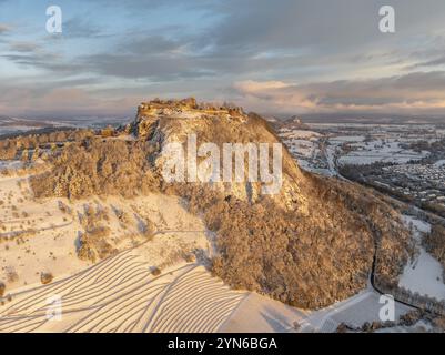 Aus der Vogelperspektive auf den schneebedeckten Hegau-Vulkan Hohentwiel mit Deutschlands größter Burgruine an einem kalten Wintermorgen, bei Sonnenaufgang, vor ihm Keim Stockfoto