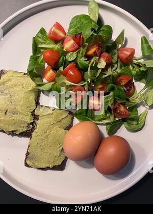 Ein nahrhaftes Frühstück mit zwei gekochten Eiern, einem lebhaften Salat aus frischen Tomaten und Gemüse sowie dunklen Brotscheiben mit cremigem Aufstrich. Stockfoto