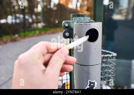 Augsburg, Bayern, Deutschland - 24. November 2024: Ein Mann hält eine brennende Zigarette vor einem öffentlichen Aschenbecher, Symbolbild für Rauchen im Freien und Tabakkonsum *** ein Mann hält eine brennende Zigarette vor einem öffentlichen Aschenbecher, Symbolbild für Rauchen im Freien und Tabakkonsum Stockfoto