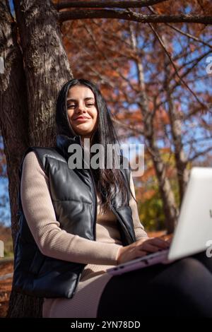 Die Studentin arbeitet an ihrem Laptop in einem Park an einem schönen Herbsttag Stockfoto