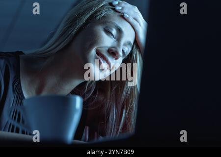 Die junge Geschäftsfrau lächelt und genießt einen Moment der Entspannung bei einer Tasse Kaffee, während sie spät in der Nacht auf ihrem Laptop arbeitet und eine Balance zwischen ihnen findet Stockfoto