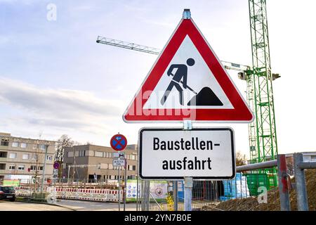 Augsburg, Bayern, Deutschland - 24. November 2024: Warnschild Baustellenausfahrt vor einer aktiven Baustelle mit Kran im Hintergrund - ein Warnhinweis zur besonderen Vorsicht im Straßenverkehr und zur Sicherung der Zufahrt zur Baustelle. *** Warnschild Baustellenausfahrt vor einer aktiven Baustelle mit Kran im Hintergrund ein Hinweis auf besondere Vorsicht im Straßenverkehr und die Sicherung der Baustellenzufahrt. Stockfoto