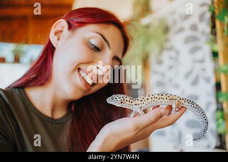 Lächelnde Frau mit rotem Haar, die einen Leopardengecko in der Hand in der Hand hält und in einem warmen und warmen Ambiente eine Liebe zu Reptilien und Natur zeigt Stockfoto