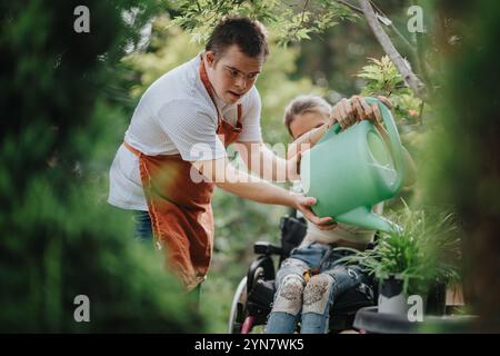 Junger Mann, der Frau in Rollstuhlwasserpflanzen im Garten hilft Stockfoto