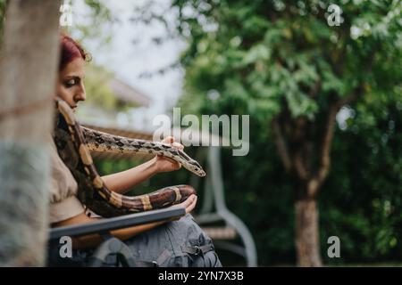 Mädchen mit großem Boa constrictor in einer ruhigen Gartenumgebung Stockfoto