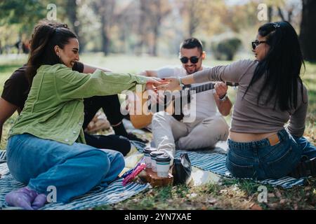 Gruppe von Freunden, die an einem sonnigen Tag ein entspannendes Picknick im Park mit einer Gitarre genießen, Lachen und Freundschaft inmitten der Natur teilen Stockfoto