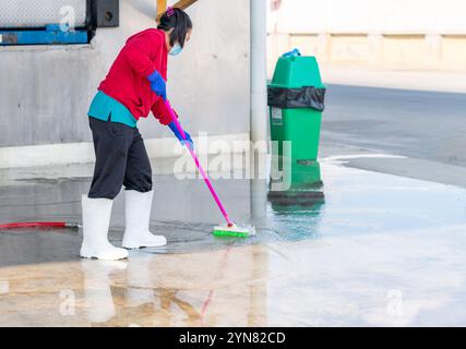 Frau, die in der Fabrik den Boden mit Mopp sauber macht. Sie trägt eine schützende Gesichtsmaske. Stockfoto