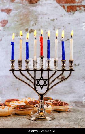 Die Menora steht hoch mit neun bunten Kerzen, umgeben von festlichen Dekorationen, während sich Familien versammeln, um Hanukka mit Freude zu feiern. Stockfoto