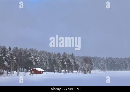 Jokkmokk, Schweden. April 2021. Ein von schneebedeckten Kiefern umgebenes Holzhaus am Ufer eines gefrorenen Sees ist in Jokkmokk, Schweden, zu sehen. (Foto: Apolline Guillerot-Malick/SOPA Images/SIPA USA) Credit: SIPA USA/Alamy Live News Stockfoto