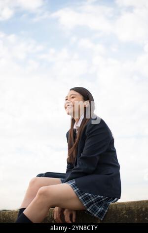 High School Mädchen in Schuluniform sitzt und lacht Stockfoto