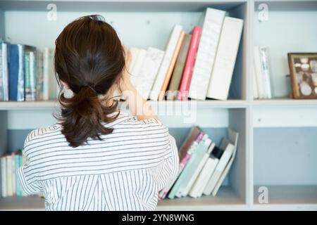 Rückansicht einer Frau, die Bücher in ein Bücherregal legt Stockfoto