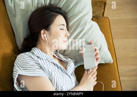 Eine Frau in ihren 20ern, die auf dem Sofa liegt und Musik hört Stockfoto