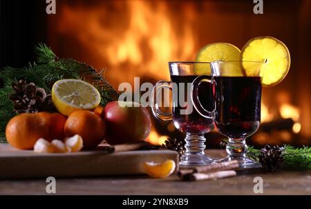 Zwei Gläser Glühwein (Gluhwein) und ein Obstteller auf dem Hintergrund eines brennenden Kamins Stockfoto