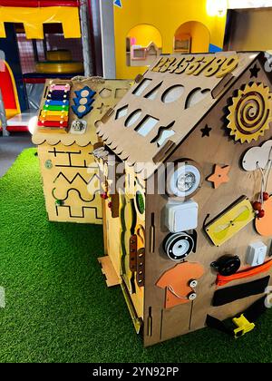 Ein hölzernes Spielhaus mit verschiedenen interaktiven Elementen, das sich in einem lebhaften Kinderspielplatz befindet. Leuchtende Farben und ansprechendes Elem Stockfoto