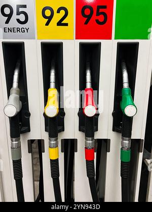 Eine Nahaufnahme von vier farbenfrohen Kraftstoffpumpendüsen an einer Tankstelle, die die Vielfalt der Kraftstoffoptionen zeigt. Das Bild vermittelt Themen wie Energie und Verkehr Stockfoto