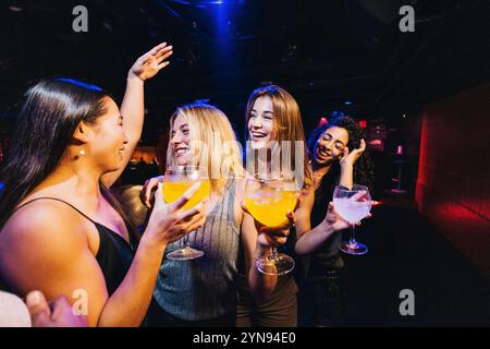 Eine Gruppe lächelnder Freunde genießt Drinks und lacht in einem Nachtclub. Die Atmosphäre ist lebendig und gesellig, mit einem Gefühl der Freude und des Feierns in der Th Stockfoto