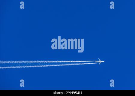 Flugzeug mit weißen Dampfpfaden, die auf einem blauen Himmel fliegen Stockfoto