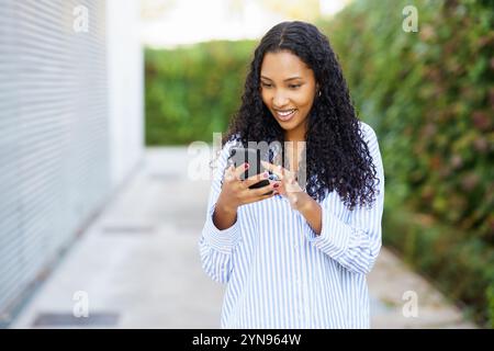 Eine junge Frau hat sich glücklich mit ihrem Smartphone beschäftigt, während sie die Umgebung im Freien genießt Stockfoto
