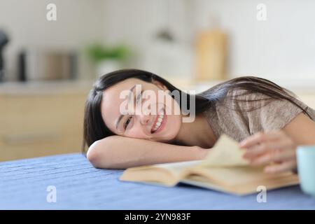 Asiatische Frau, die ein Buch liest, sieht dich in der Küche zu Hause an Stockfoto