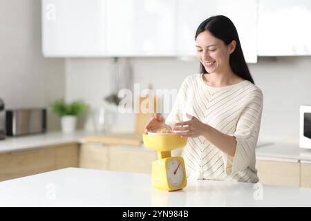 Glückliche asiatische Frau, die in der Küche zu Hause Essen mit Waage wägt Stockfoto