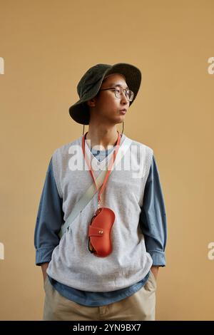 Vertikale Taille oben Porträt eines asiatischen Mannes, der sackiges lässiges Outfit mit Accessoires vor schlichtem Hintergrund trägt Stockfoto