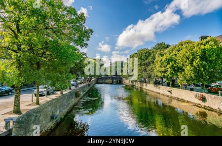 Eine malerische Szene mit einer bezaubernden Steinbrücke mit Blumen über einem ruhigen Fluss in einem malerischen europäischen Dorf mit historischem Archit Stockfoto