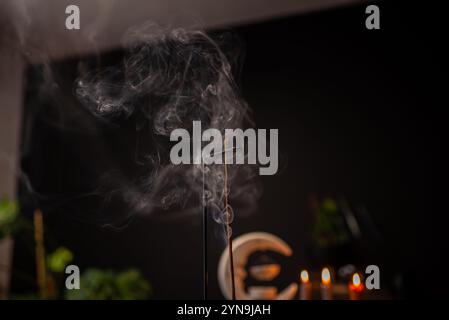 Rauchlocken von Räucherstäbchen in Holzhalterung für Entspannungs- und Meditationsübungen, schwarzer Hintergrund. Aromatherapie-Sitzung mit brennendem Duftstäbchen Stockfoto