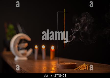 Rauchlocken von Räucherstäbchen in Holzhalterung für Entspannungs- und Meditationsübungen, schwarzer Hintergrund. Aromatherapie-Sitzung mit brennendem Duftstäbchen Stockfoto