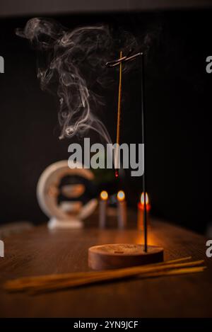 Rauchlocken von Räucherstäbchen in Holzhalterung für Entspannungs- und Meditationsübungen, schwarzer Hintergrund. Aromatherapie-Sitzung mit brennendem Duftstäbchen Stockfoto