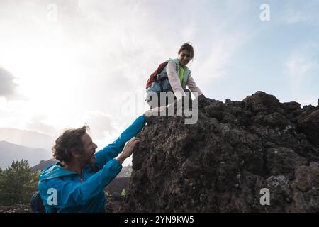 Junge aktive Paare wandern in den Bergen und helfen sich gegenseitig beim Aufstieg in felsiges Gelände während des Abenteuers. Konzepte von Support, Teamwork und Outdoor-Lifestyle Stockfoto