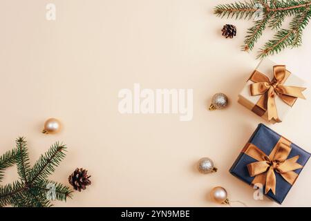 Minimaler weihnachtlicher Flachbau mit Tannenzweigen, Geschenkboxen mit goldenen Bändern und festlichen Ornamenten auf beigefarbenem Hintergrund. Draufsicht, Kopierraum. Stockfoto
