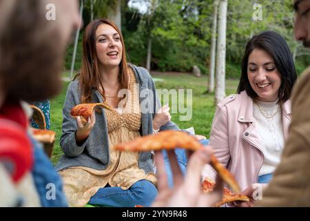 Ehrlicher Moment, in dem männliche und weibliche Freunde Pizza im Freien genießen. Natürliche Ausdrucksformen von Freude und Freundschaft bei zwanglosen Wochenendversammlungen im Frühling Stockfoto