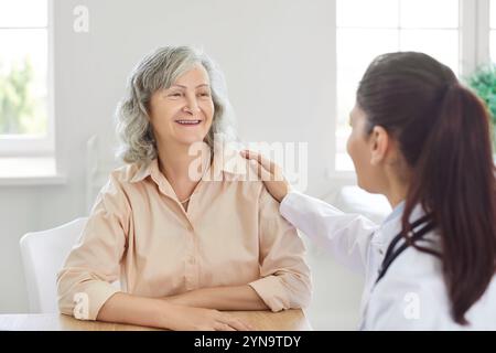 Der Arzt spricht mit einer älteren Patientin und legt ihre Hand auf ihre Schulter, um sie zu stützen und zu beruhigen Stockfoto