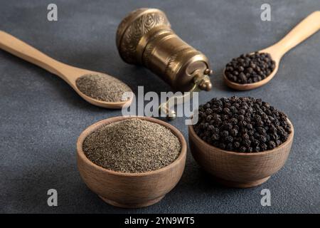 Schwarze Pfeffer, gemahlener schwarzer Pfeffer und Metallmühle auf schwarzem Hintergrund Stockfoto