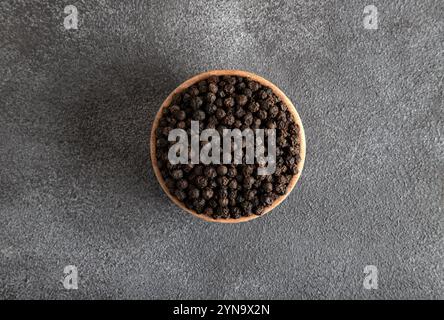 Schwarze Pfefferkörner in Holzschale auf grauem Betonhintergrund Stockfoto