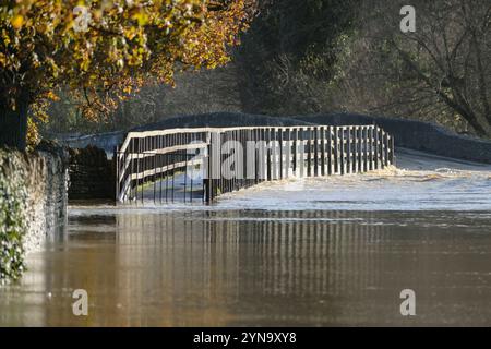 Lacock, Wiltshire, Großbritannien. November 2024. Der starke Regen des Sturms Bert hat den Fluss Avon in Lacock überschwemmt. Die Straße ist für alle bis auf die größten Fahrzeuge unpassierbar. Dieser Standort wird mehrmals im Jahr überschwemmt, aber heute ist das Wasser viel höher, und das Hochwasser erstreckt sich normalerweise nicht über den Damm hinaus, sondern hat es heute getan. Schnell fließendes Hochwasser Stockfoto