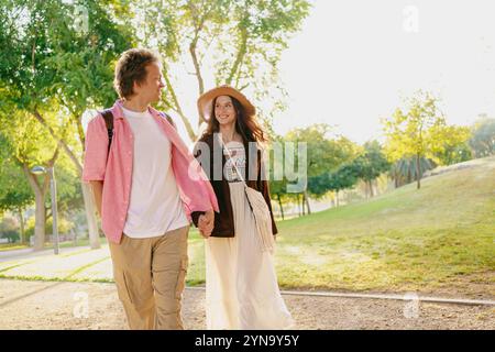 Ein Paar schlendert Hand in Hand durch einen wunderschönen, sonnendurchfluteten Park voller Grün Stockfoto