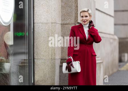 Porträt stilvolle Frau im Burgundermantel in der City Street mit modischer Kleidung Weißer Rollkragenpullover, graue Jeans, weiße Tasche tragen. Bestätigen Stockfoto