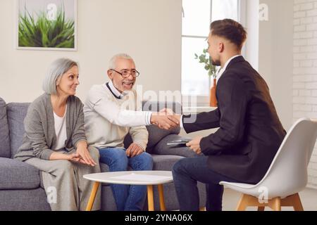 Älteres Ehepaar, das mit Immobilienmaklern einen Vertrag über ihren neuen Hauskauf abschließt. Handschlag symbolisiert Vertrauen und Zufriedenheit Stockfoto