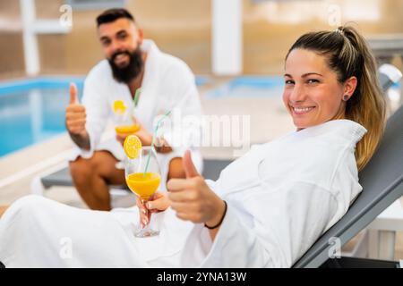 Junge glückliche Paare entspannen sich am Swimmingpool. Mann und Frau genießen im Spa-Center. Sie trinken Saft. Stockfoto
