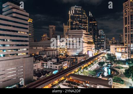 Ein nächtlicher Blick auf Bangkoks pulsierende Stadtlandschaft mit beleuchteten Gebäuden, belebten Straßen und farbenfrohen Ampeln Stockfoto