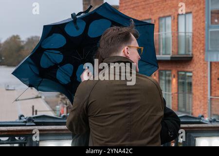 Windsor, Großbritannien. November 2024. Ein Mitglied der Öffentlichkeit benutzt einen kaputten Schirm, um sich vor Wind und Regen auf der Windsor Bridge während Sturm Bert zu schützen. Eine gelbe Windwarnung wurde für Südengland und Teile von Wales ausgegeben. Quelle: Mark Kerrison/Alamy Live News Stockfoto