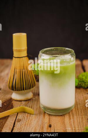 Eine Nahaufnahme eines Bambus-Matcha-Schneebesen auf einem Matcha-Tisch, der Achtsamkeit und Tradition symbolisiert. Ein volles Glas gefrorener Matcha Latte Stockfoto
