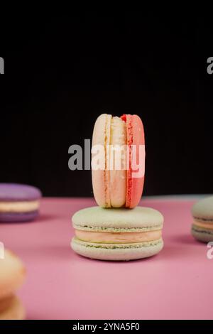 Eine bunte Auswahl an Macarons auf einer Basis mit einem weichen rosa Hintergrund. Dieses delikate französische Gebäck zeigt Eleganz und Geschmack, perfekt für Stockfoto