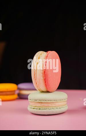 Eine bunte Auswahl an Macarons auf einer Basis mit einem weichen rosa Hintergrund. Dieses delikate französische Gebäck zeigt Eleganz und Geschmack, perfekt für Stockfoto