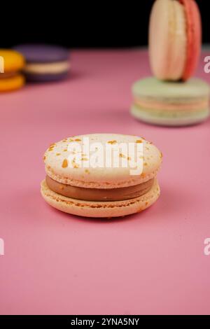 Eine bunte Auswahl an Macarons auf einer Basis mit einem weichen rosa Hintergrund. Dieses delikate französische Gebäck zeigt Eleganz und Geschmack, perfekt für Stockfoto