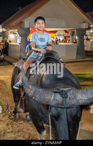 Kind genießt eine spielerische Fahrt auf einem Büffel auf einem Nachtmarkt Stockfoto