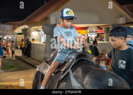 Kind genießt eine spielerische Fahrt auf einem Büffel auf einem Nachtmarkt Stockfoto