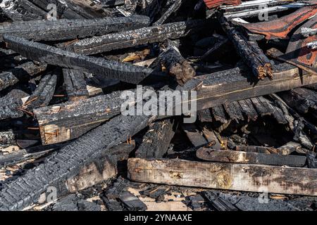 Haufen verkohlter Holzbretter nach dem Feuer. Haufen verbrannter Holzdielen an einem sonnigen Tag. Feuerunfall- und Kohlekonzept. Stockfoto