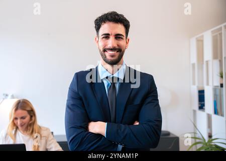 Selbstbewusster Geschäftsmann, der mit überkreuzten Armen in einem modernen Büro mit Kollegen steht Stockfoto